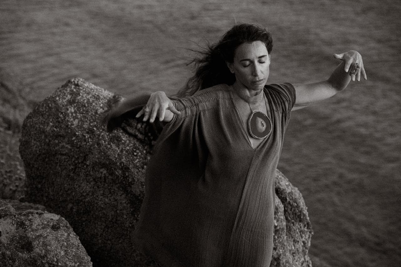 Arms open on a rock above the water, eyes closed, in black and white.